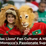 Passionate Morocco national team supporters waving flags, singing chants, and filling stadium stands with red and green colors during an Atlas Lions match.