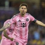 Lionel Messi in pink Inter Miami jersey with outstretched arms.