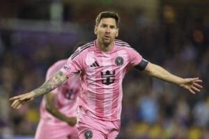 Lionel Messi in pink Inter Miami jersey with outstretched arms.